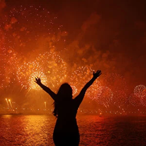 A woman celebrates the New Year as she watches fireworks exploding above Copacabana beach