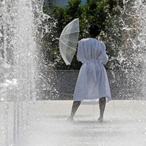 A woman cools off in water fountains in a park as hot summer temperatures hit Paris