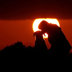 A woman gives her dog a kiss as they watch the sunset at Anchor Bay outside Mellieha