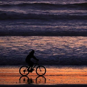 A woman rides her bicycle at sunset on a beach in La Serena