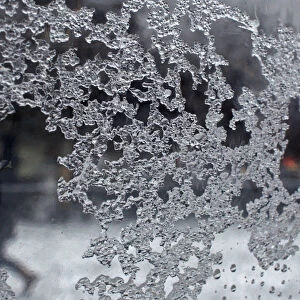 A woman is seen walking in the background through a sheet of glass, on which ice particles