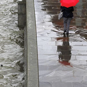 A woman shelters under her umbrella as she walks alongside the River Thames during