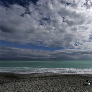 A woman sits on the beach on the Promenade des Anglais in Nice