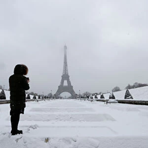 A woman takes pictures of the Eiffel Tower in Paris under the falling snow as winter