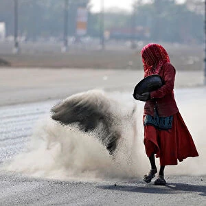 A woman throws a mixture of black ash, cement, concrete powder and ordinary dust over