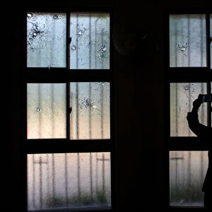 A woman uses her mobile phone to take pictures of bullet holes in windows damaged during