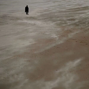 A woman walks along the beach through blowing sand in New Brighton