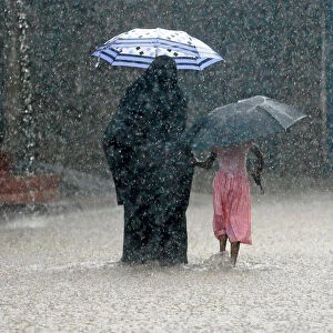 A woman walks with a girl along a flooded road in the heavy rains in Malwana