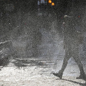 A woman walks through a gust of blowing snow in frigid cold temperatures though downtown