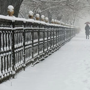 A woman walks along a park fence during a snowfall in Almaty