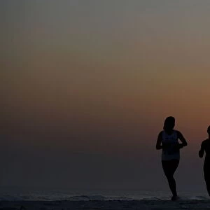 Women run during sunset on Barra da Tijuca beach in Rio de Janeiro