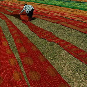 A worker lays batik cloth out on the grass to dry in Solo