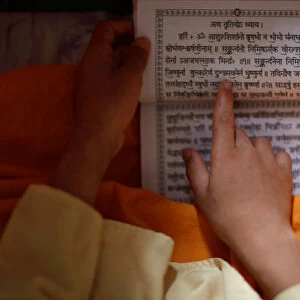 A young Hindu priest reads a holy book with prayers written on it during the Janai
