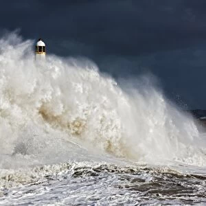 Coastal resort town seafront and lighthouse bombarded by waves during storm, Porthcawl Pier, Porthcawl