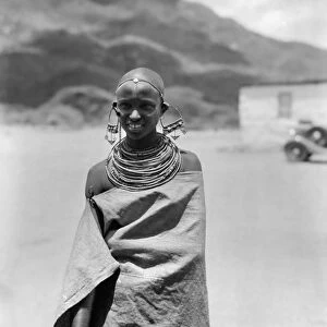 TANGANYIKAN GIRL, 1936. A girl wearing large earrings, numerous neck rings, and a cloak