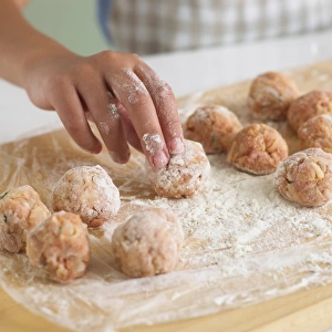 Woman rolling minced meatballs into flour