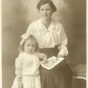 Pretty girl, mother or governess, showing photos to young child (b / w photo)