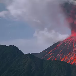 Reventador Volcano erupting at night, red hot boulders ejected from crater rolling down