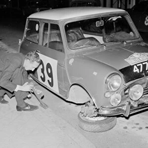 Rally driver raymond Baxter repalces the wheel of his Mini car which was removed by some