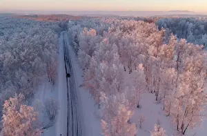 An aerial view shows a car driving along a forest road during sunset in the Siberian