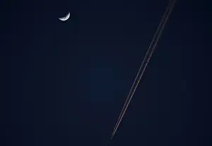 An aeroplane flies past a crescent moon at dusk in Alcala de Henares