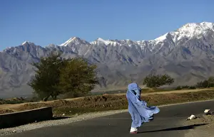 An Afghan woman in a burqa walks along a road on a windy day on the outskirts of Kabul