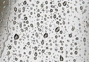 An airplane waiting to depart the gate is reflected in rain drops on a window at Logan