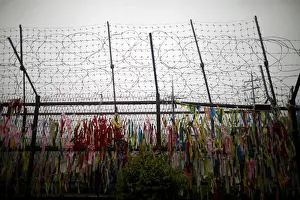 A barbed wire fence is decorated with ribbons bearing messages wishing for unification of