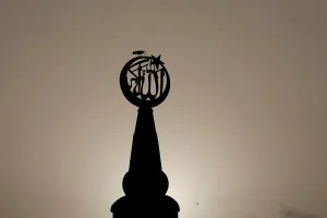 A bird sits on a religious sign on a mosque, silhouetted against the setting sun in A bird sits on a religious sign on a mosque, silhouetted against the setting sun in