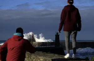 Two boys look at waves as they crash against a lighthouse in the port town of Viavelez