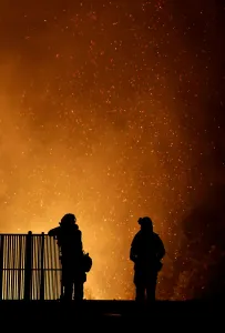 Wildfire Prints: Burning embers swirl around firefighters as they stand guard at a home while battling