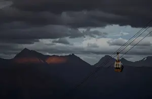 A cable car is pictured with Caucasus mountains during sunset in the background outside