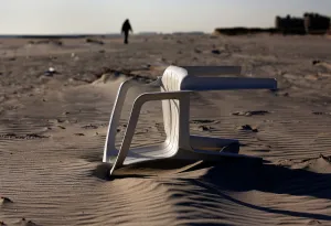 A chair is seen lying in the sand on the beach as a silhouette of a man walks in Atlantic A chair is seen lying in the sand on the beach as a silhouette of a man walks in Atlantic