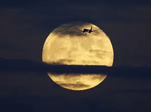 Images Dated 2014 October: A commercial airliner crosses the path of a rising full moon as it comes in to land