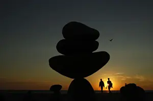 A couple walk past stone sculptures built on Moshup Beach as the sun sets in Aquinnah