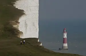 United Kingdom Prints: A couple walk along the Seven Sisters cliffs close to the Beachy Head lighthouse near Eastbourne