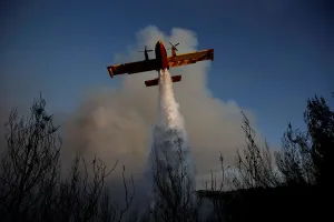 Greece Prints: A firefighting airplane makes a water drop as a wildfire burns near the village of