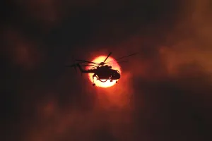 Greece Prints: A firefighting helicopter flies in front of the setting sun as a wildfire burns near