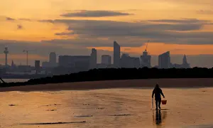 Weather Prints: A fisherman digs for bait in front of the Liverpool skyline on the beach at New Brighton