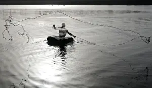 India Prints: Fisherman floating on a rubber tube throws a net to catch fish from the waters of
