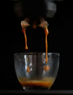 Freshly ground Arabica coffee drips from a domestic coffee machine to make an espresso