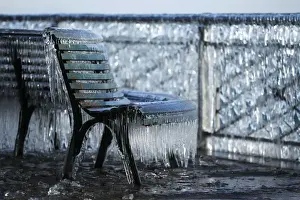 A frozen public bench is seen next to a lake side due to the heavy wind conditions