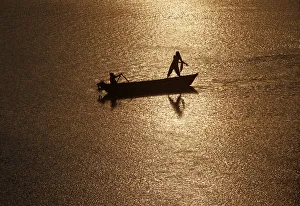 India Prints: Girls are silhouetted against the rising sun as they fish in the waters of the Ganges