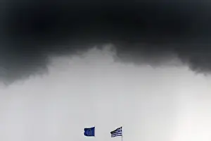A Greek national flag and an EU flag flutter under storm clouds in Athens