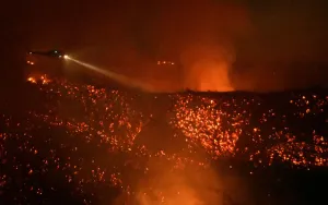 Wildfire Prints: A helicopter flies above glowing embers as it makes a water drop run at the Old Fire