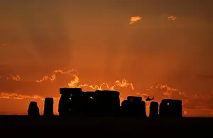 A helicopter flies behind the Stonehenge stone circle during sunset in southwest Britain