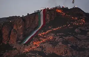 Iraqi Kurdish people carry fire torches up a mountain where a giant flag of Iraq s