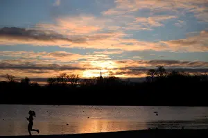 United Kingdom Prints: A jogger runs past the Round Pond in Kensington Gardens during sunrise in London
