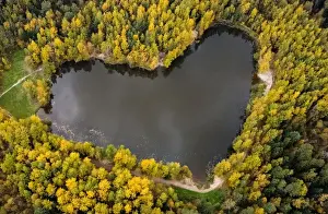 : A lake in a shape of a heart is seen surrounded by autumn-coloured trees outside