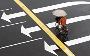 A man crosses an intersection on his bicycle while holding an umbrella as it rains A man crosses an intersection on his bicycle while holding an umbrella as it rains